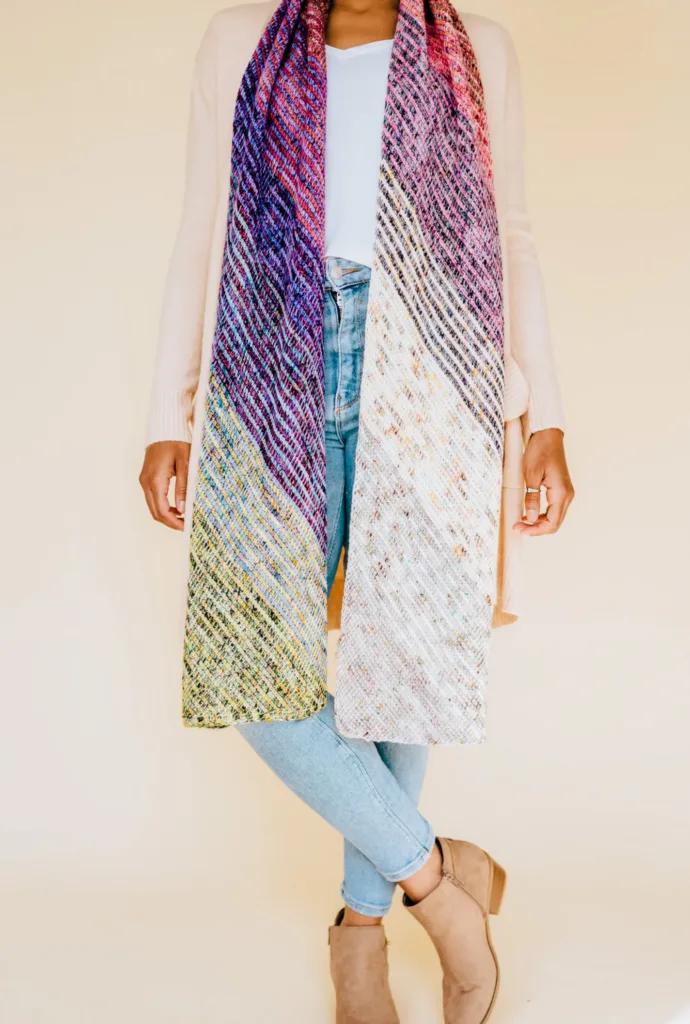 Model wearing the Adventurous Scarf by TL Yarn Crafts, a long Tunisian crochet scarf with a diagonal rainbow gradient made from colorful yarn advent minis.