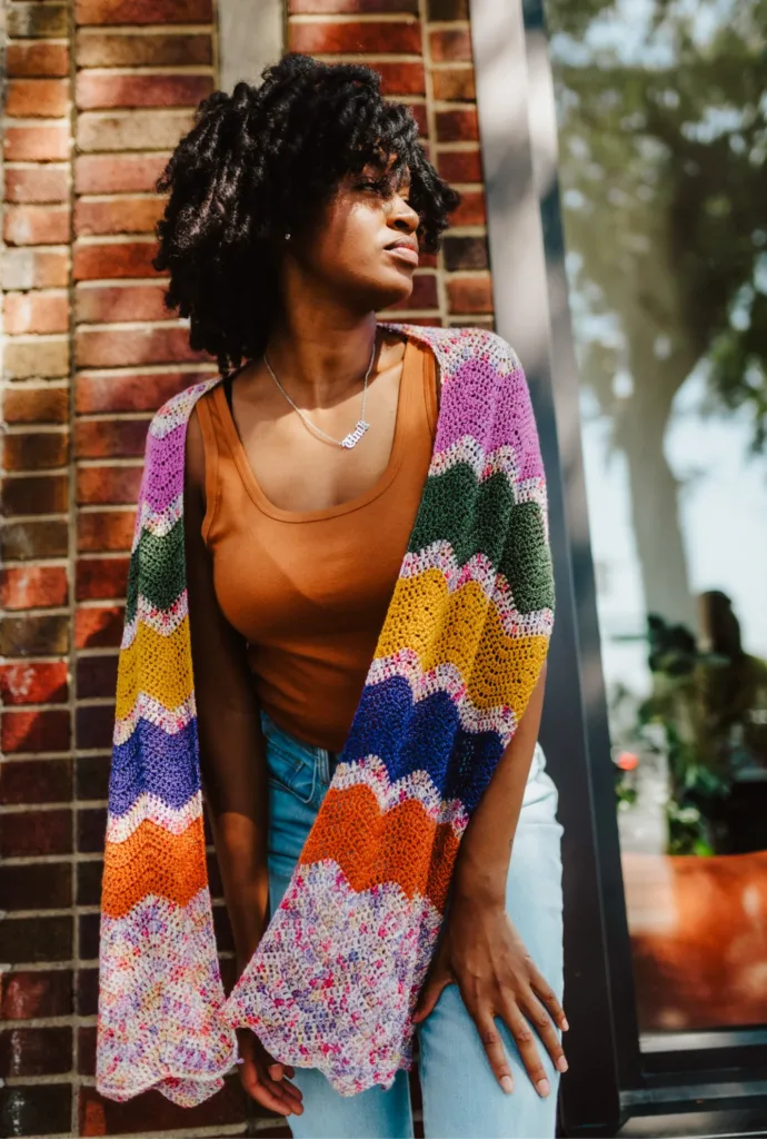 Model wearing the Bouquet Scarf by TL Yarn Crafts, a colorful ripple-stitch crochet scarf made with bright yarn mini skeins.