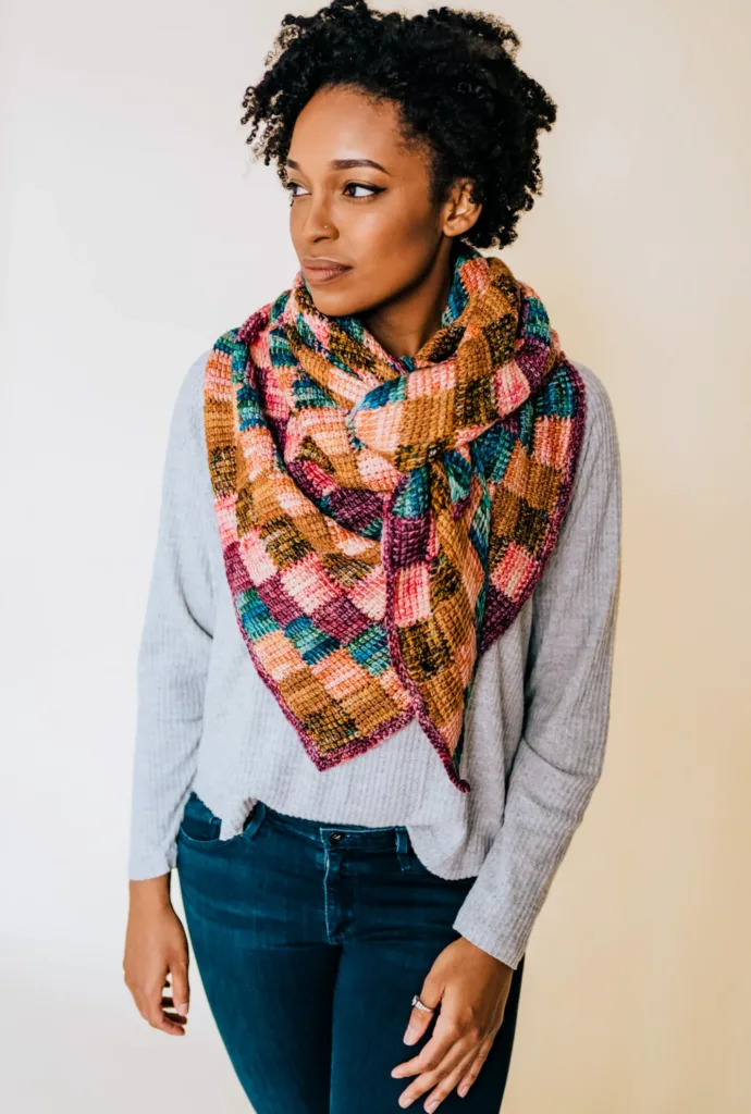 Model wearing the Entrelac & Key Shawl by TL Yarn Crafts, a colorful patchwork-style Tunisian crochet wrap made from small entrelac blocks perfect for minis.