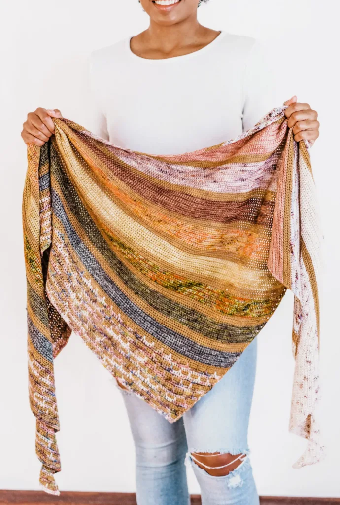 Model holding the Fairbanks Shawl by TL Yarn Crafts, a large triangular Tunisian crochet shawl worked in soft striped rows using advent mini skeins.