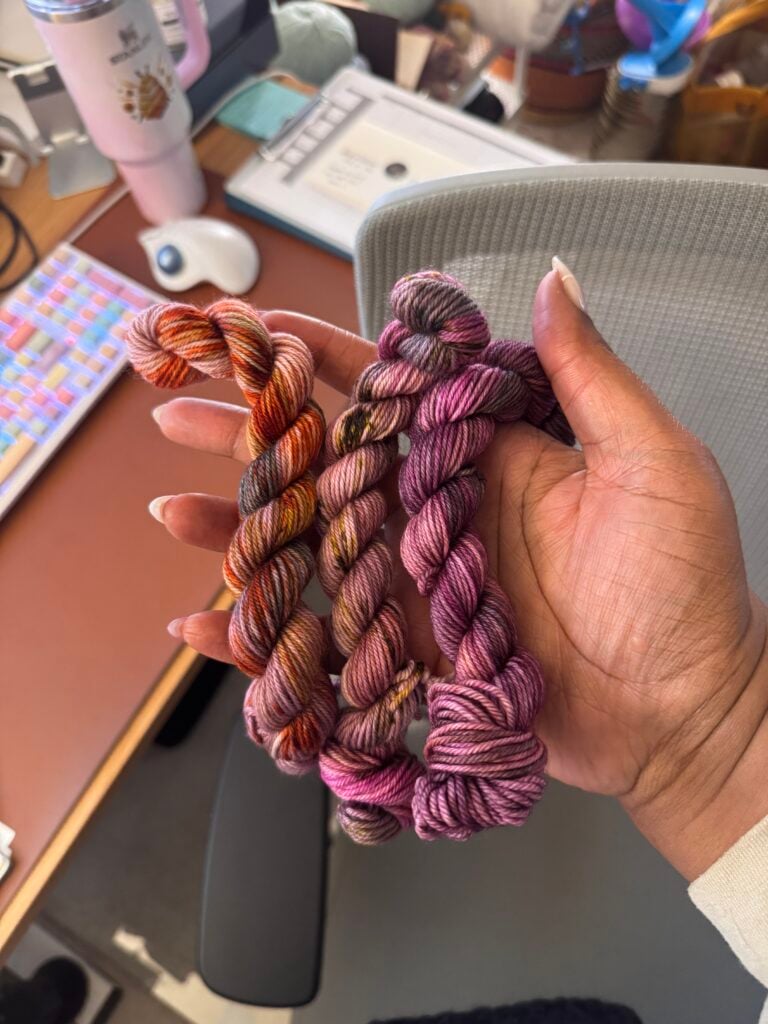 Hand holding variegated yarn advent mini skeins in warm and purple colors.