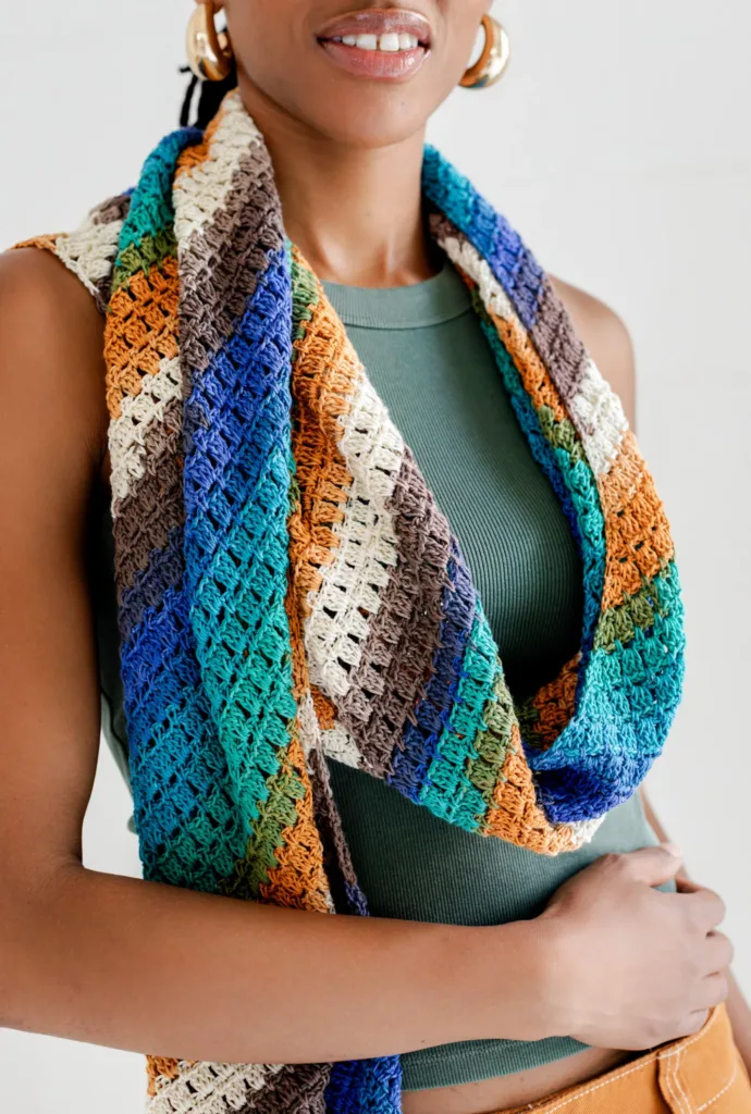 Close-up of a model wearing the Kelli Bias Scarf by TL Yarn Crafts, a lightweight crochet scarf worked on the diagonal with colorful striped yarn perfect for self-striping yarn and minis.
