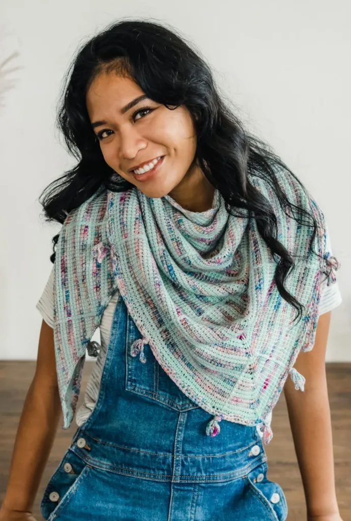 Model wearing the Sylvie Shawl by TL Yarn Crafts, a lightweight triangular Tunisian crochet shawl made with soft speckled yarn minis and tiny tassel accents.