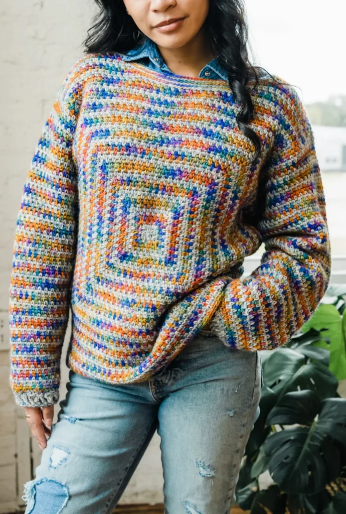 Model wearing the Willow Sweater by TL Yarn Crafts, a multicolored crochet sweater featuring a linen-stitch square on the front and striped sleeves.