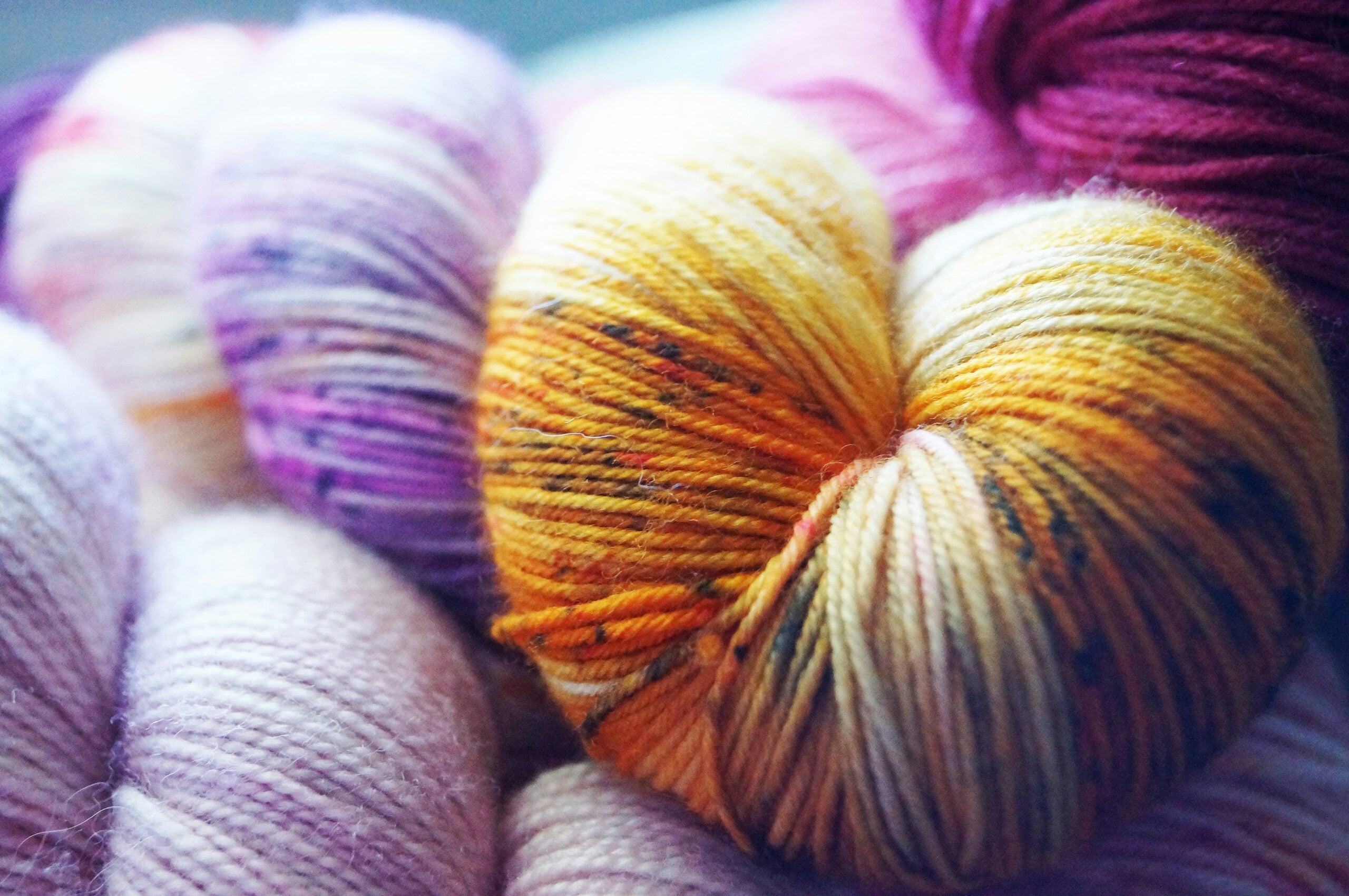 Close-up of colorful hand-dyed yarn skeins in warm yellow, purple, and pink tones, ideal for stash-first crochet projects.