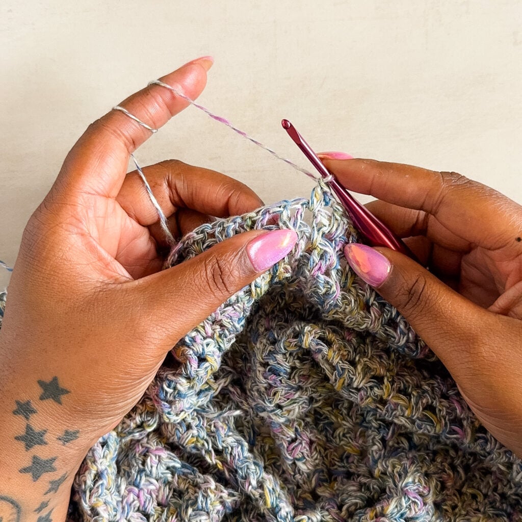Crocheter wrapping yarn twice around the index finger, creating a tighter yarn hold.
