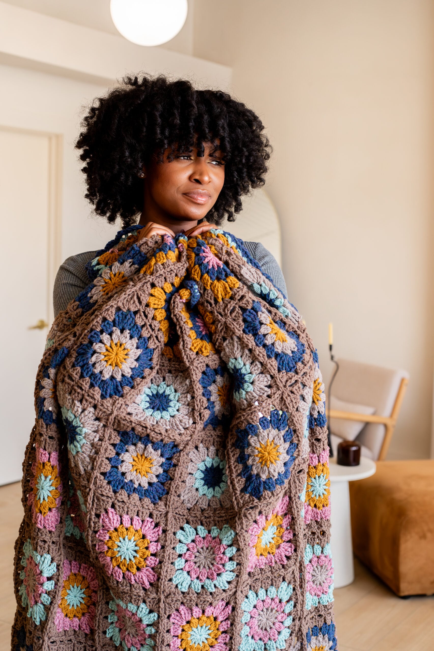 Woman cuddling a colorful granny square blanket - free pattern + tutorial video available