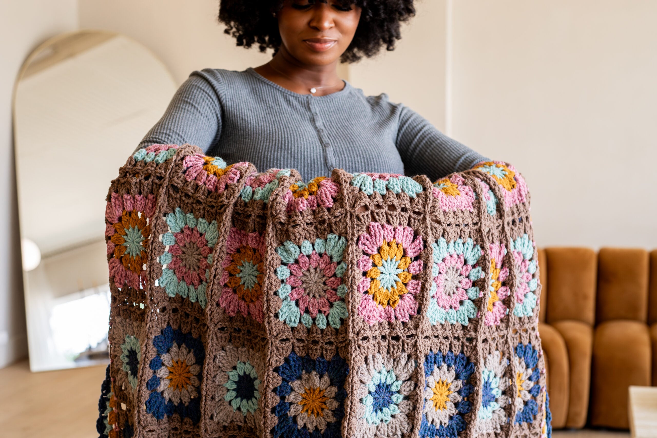 Woman with colorful crochet granny square blanket draped over her arms - make yours with the free crochet pattern + tutorial video