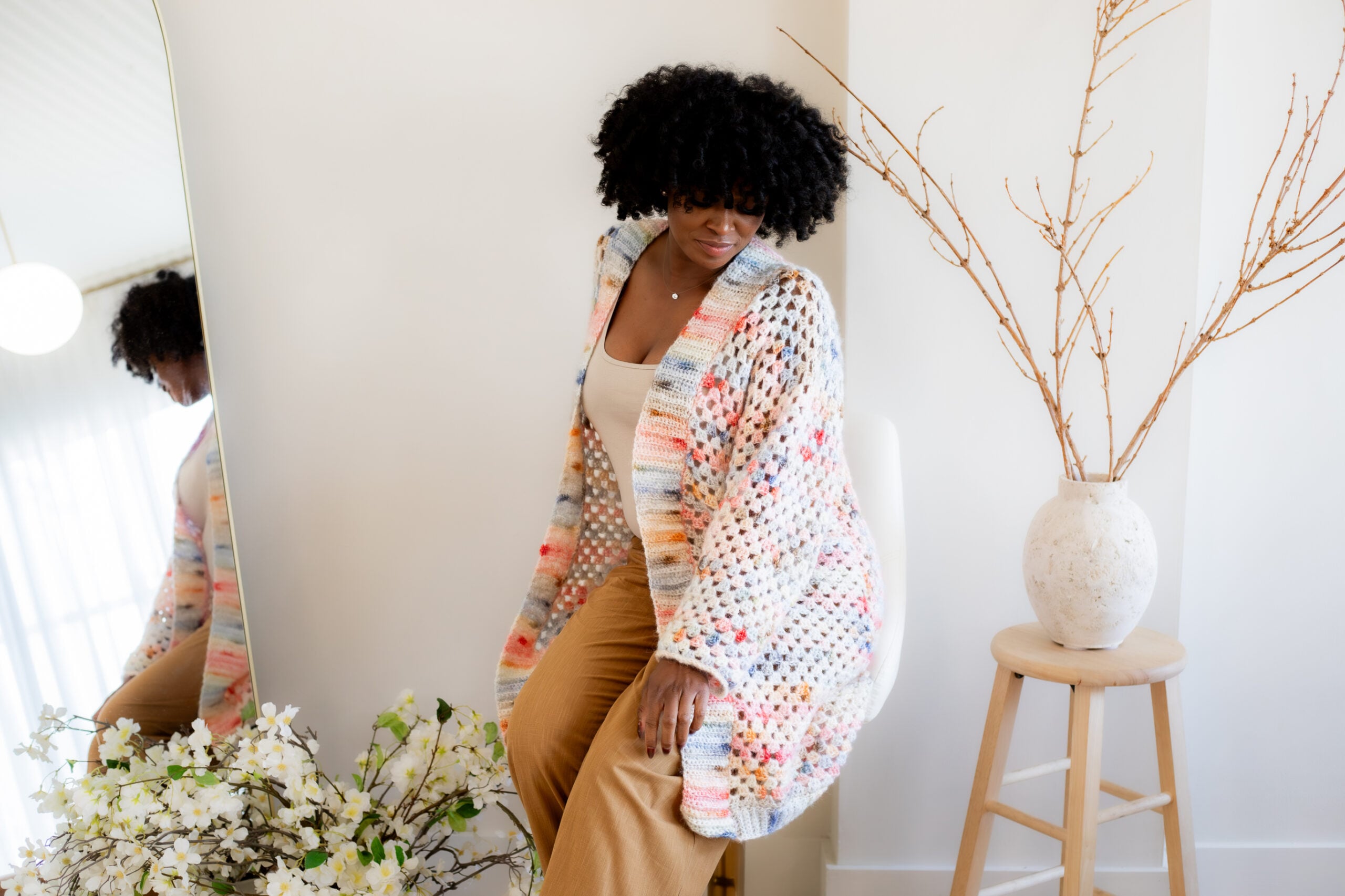 Woman sitting down, wearing a pink and blue granny square cardigan - free crochet pattern