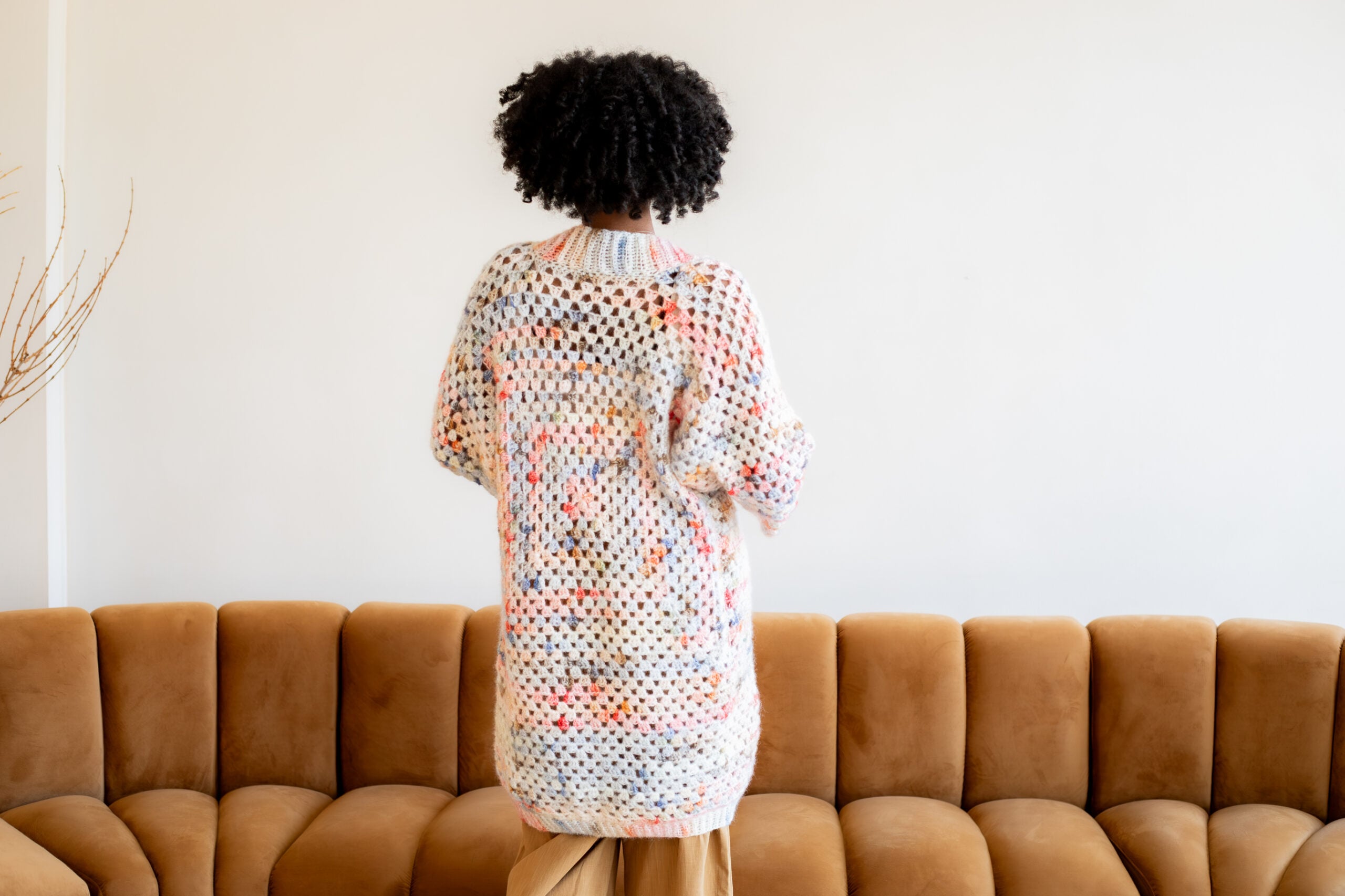 Woman with her back turned, wearing a pink and blue granny square cardigan - free crochet pattern