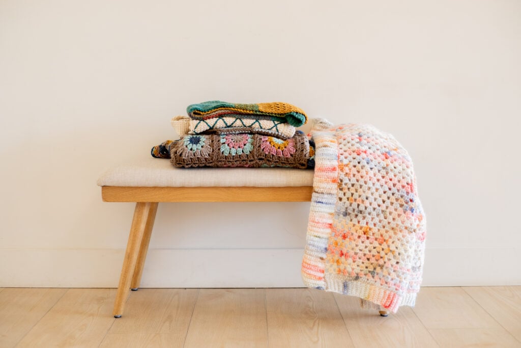 Stack of hand-crocheted pieces, including a pink and blue granny square cardigan - free crochet pattern
