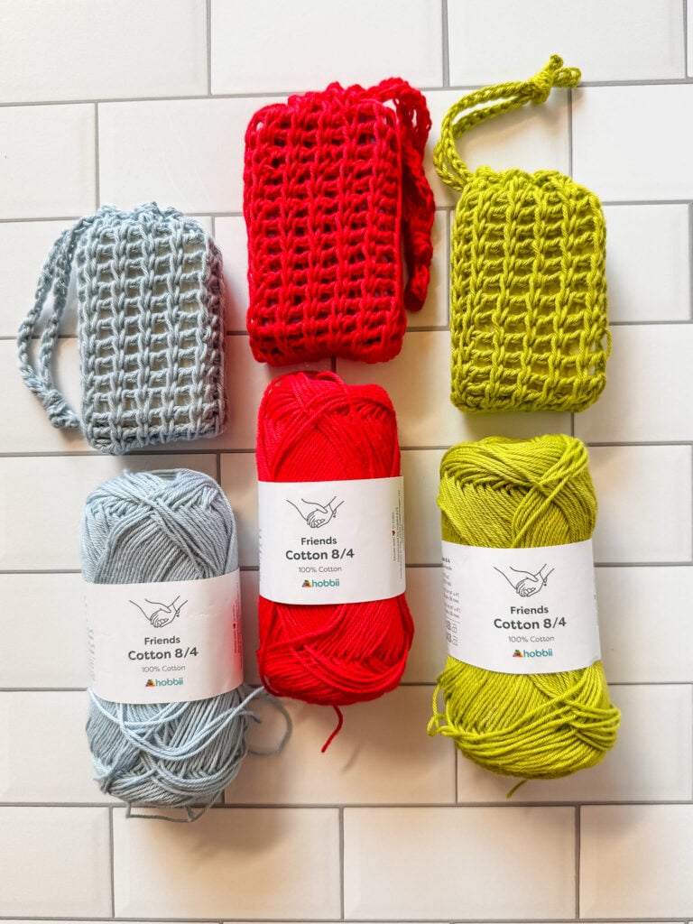 Light blue, red and green Hobbii Friends Cotton 8/4 yarn displayed with matching Tunisian crochet soap savers on white tile.
